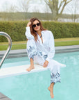 Woman in a white outfit with blue patterns sitting by a pool.