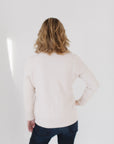 Back view of Eleanor Leftwich wearing The Perfect Cardigan in cream paired with dark denim jeans, facing a white background.