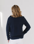 Back view of Eleanor Leftwich wearing the Navy Perfect Crewneck sweater paired with white denim jeans against a white background.