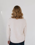 Back view of Eleanor Leftwich wearing the cream Perfect Crewneck sweater paired with dark denim jeans against a white background.