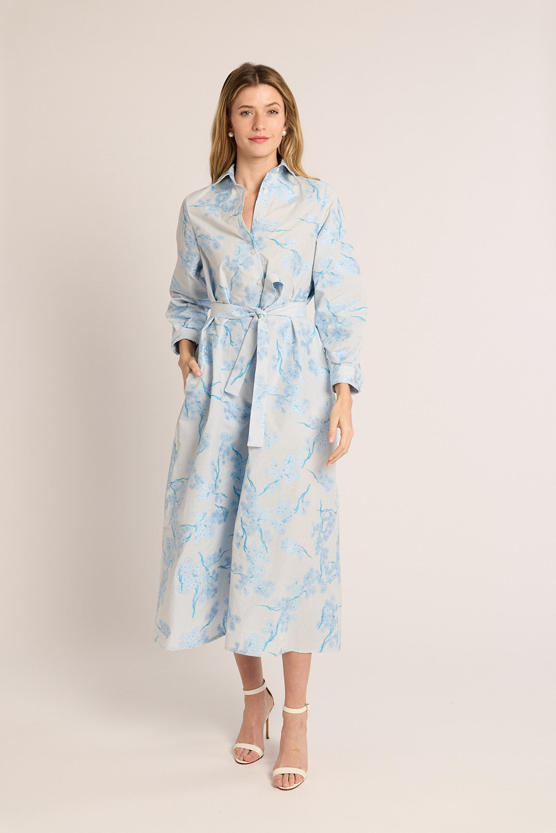 Woman wearing a light blue floral dress with a belt on a white background