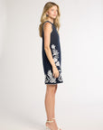 Woman modeling a black dress with fern detailing and heels on a white backdrop