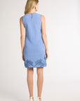 A woman standing to the back wearing a blue hand-crochet dress with blue fern detailing on a white background