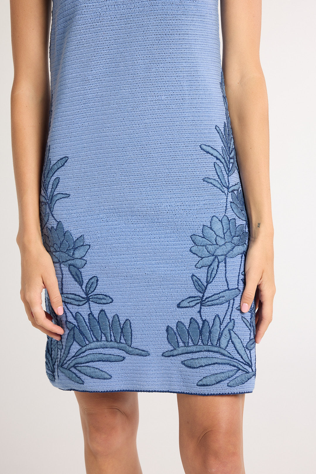 A woman wearing a hand-crochet blue dress with blue floral embroidery on a white background