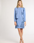 Woman modeling a blue jacket with fern detailing over the matching dress on a white backdrop