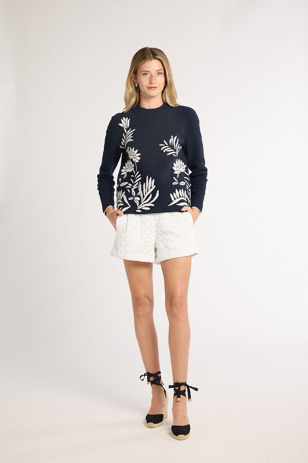 Woman wearing a black long sleeve sweater with white fern detailing on the front on a white backdrop