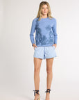 A woman wearing a light blue crewneck with blue fern detailing on a white backdrop