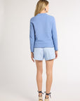 Woman modeling a light blue hand-crochet sweater and wearing heels in a studio
