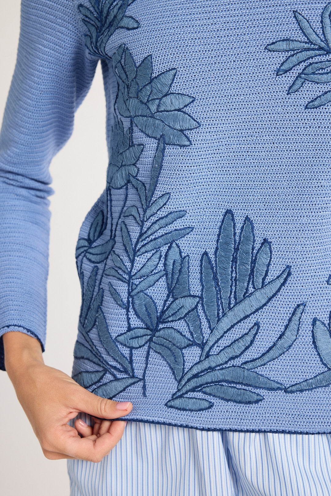 Close up of blue crewneck with blue fern embroidery on a white background