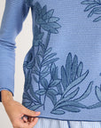Close up of blue crewneck with blue fern embroidery on a white background