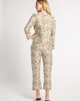 A woman modeling a long-sleeve cropped jumpsuit with an intricate beige and brown floral scroll pattern, shown from the back against a light gray studio background.