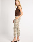 A woman modeling a sleeveless brown top and high-waisted cropped trousers with an intricate beige and brown paisley pattern, paired with dark brown pointed-toe mule heels, against a plain light gray studio background.
