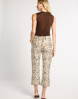 A woman shown from the back wearing a sleeveless brown top and patterned cropped pants with an abstract floral print in beige, brown, and black, paired with black heels, against a light gray studio background.