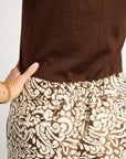 A close-up of a person wearing a solid brown top and brown-and-cream patterned pants, with a hand in the pocket of the pants.
