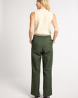 A woman is shown from the back wearing a cream cable-knit sleeveless top and dark olive green wide-leg trousers, standing against a light gray studio background.