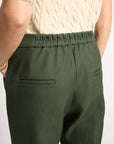 A close-up back view of a person wearing olive green trousers with an elastic waistband and side pockets, paired with a cream cable-knit top against a plain light background.