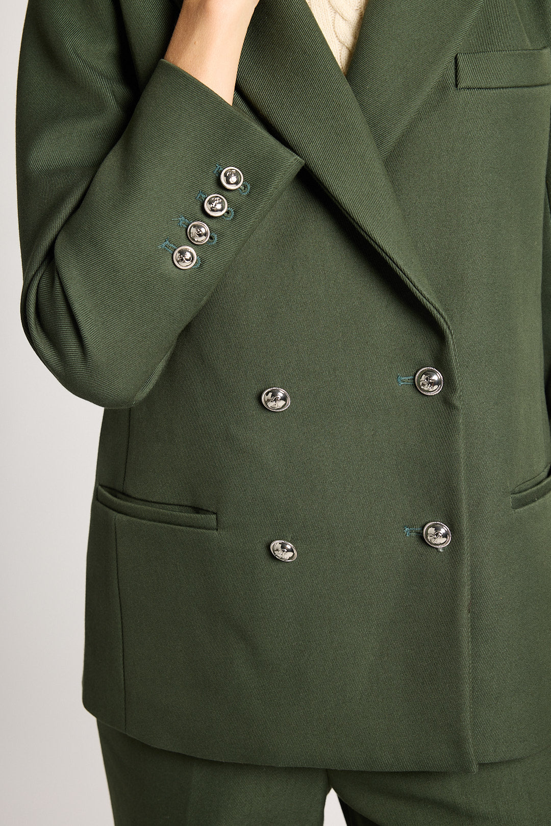 Close-up of a dark olive green double-breasted blazer with silver buttons, worn by a model.