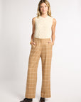 A woman modeling a sleeveless cream cable-knit top and tan windowpane plaid wide-leg trousers with black leather loafers, shot against a light gray studio background.