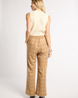 A woman is shown from the back wearing tan wide-leg trousers with a white windowpane check pattern and a cream cable-knit sleeveless top, standing against a light gray studio background.