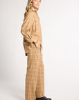 A woman modeling a matching beige and white windowpane plaid lounge set, featuring a long-sleeve top and wide-leg trousers, paired with black leather loafers against a plain white studio background.