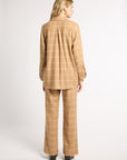A woman viewed from the back wearing a tan and beige windowpane plaid blazer and matching wide-leg trousers, standing against a light gray studio background.