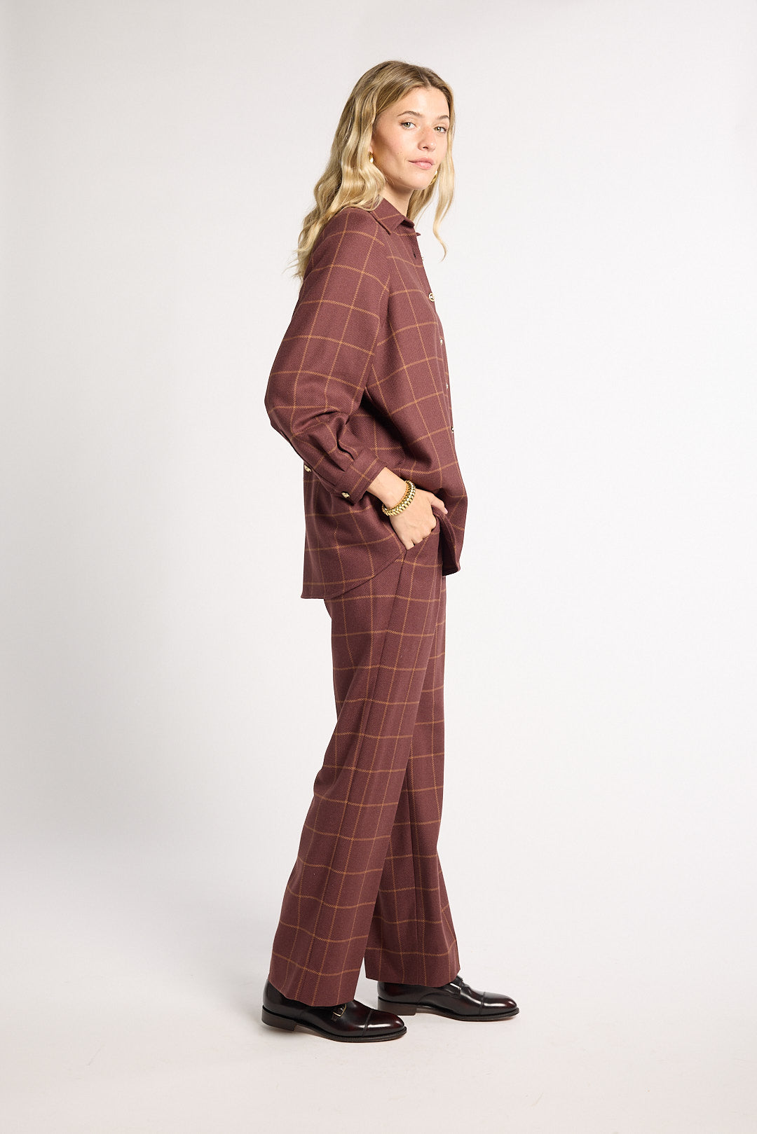 A woman modeling a matching two-piece plaid lounge set in a dusty rose-brown color, featuring a long-sleeve button-up shirt and wide-leg trousers, paired with black leather shoes against a plain white studio background.