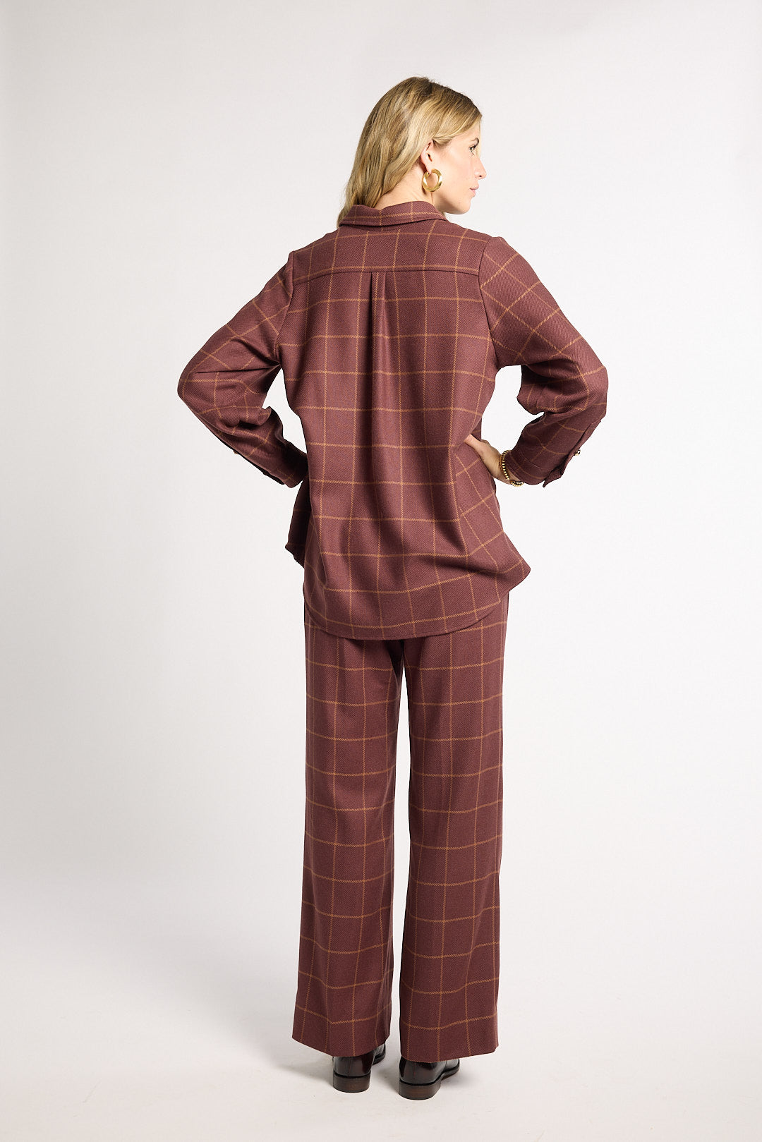 A woman is shown from the back wearing a matching two-piece plaid lounge set in a dusty rose-brown color. The set includes a long-sleeve button-up shirt and wide-leg trousers, photographed against a plain light gray studio background.