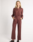 A woman modeling a brown and burgundy windowpane plaid long-sleeve button-up shirt and matching wide-leg trousers, styled with black leather loafers against a plain white studio background.