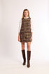 Woman wearing a plaid tweed dress with a white shirt and brown knee-high boots on a white background