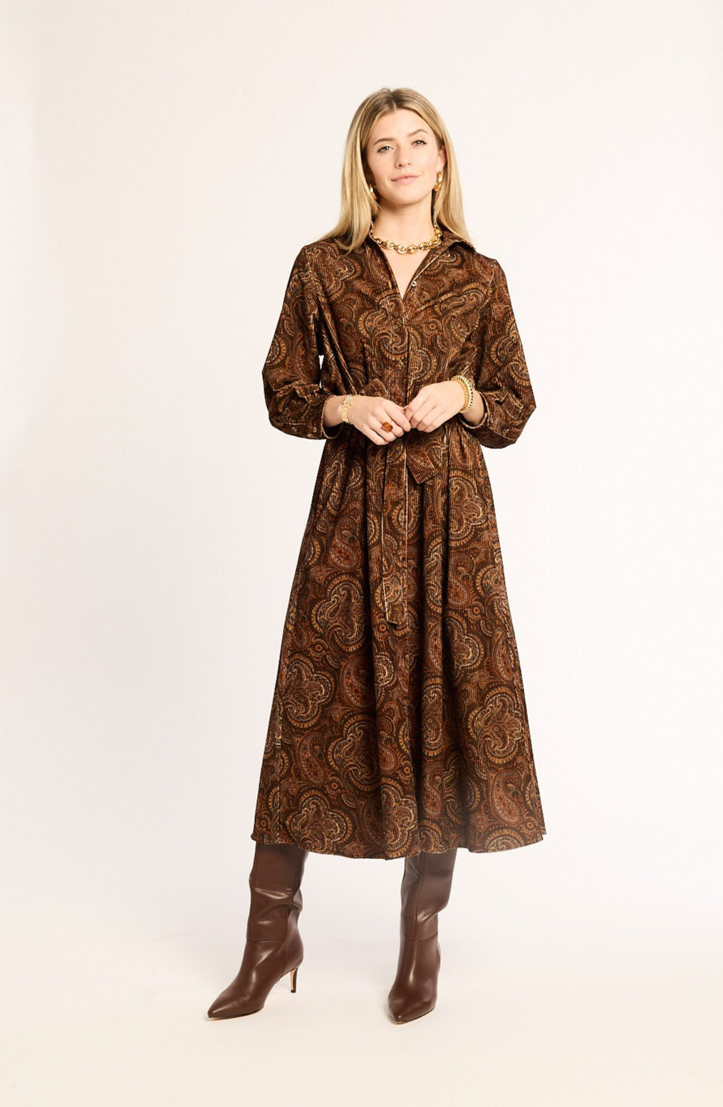 Woman wearing a brown patterned dress and boots on a white background