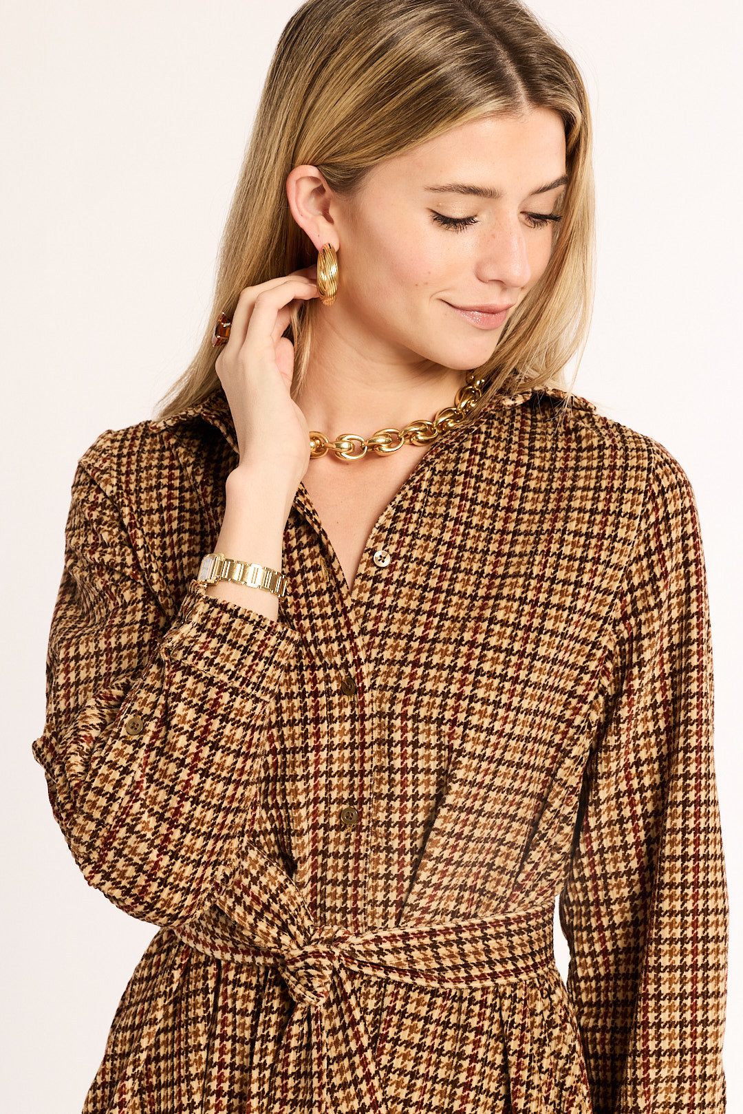 Woman wearing a brown checkered dress with gold jewelry on a white background