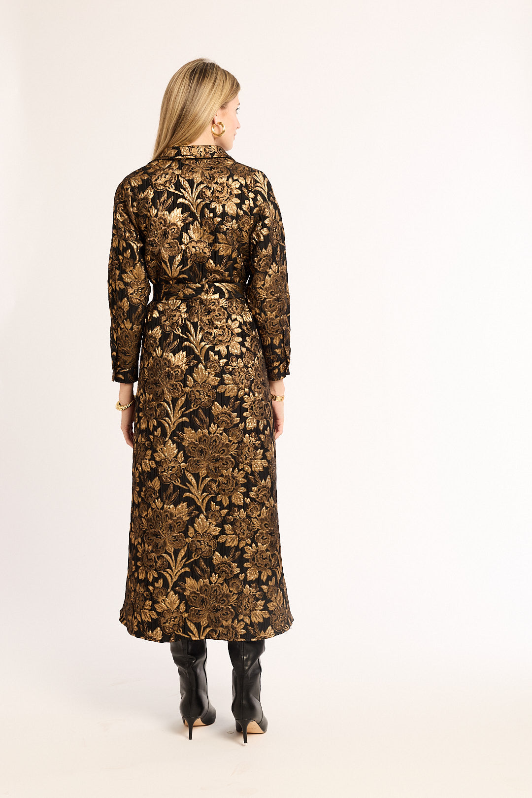 Woman wearing a long floral dress with a gold and brown pattern on a white background