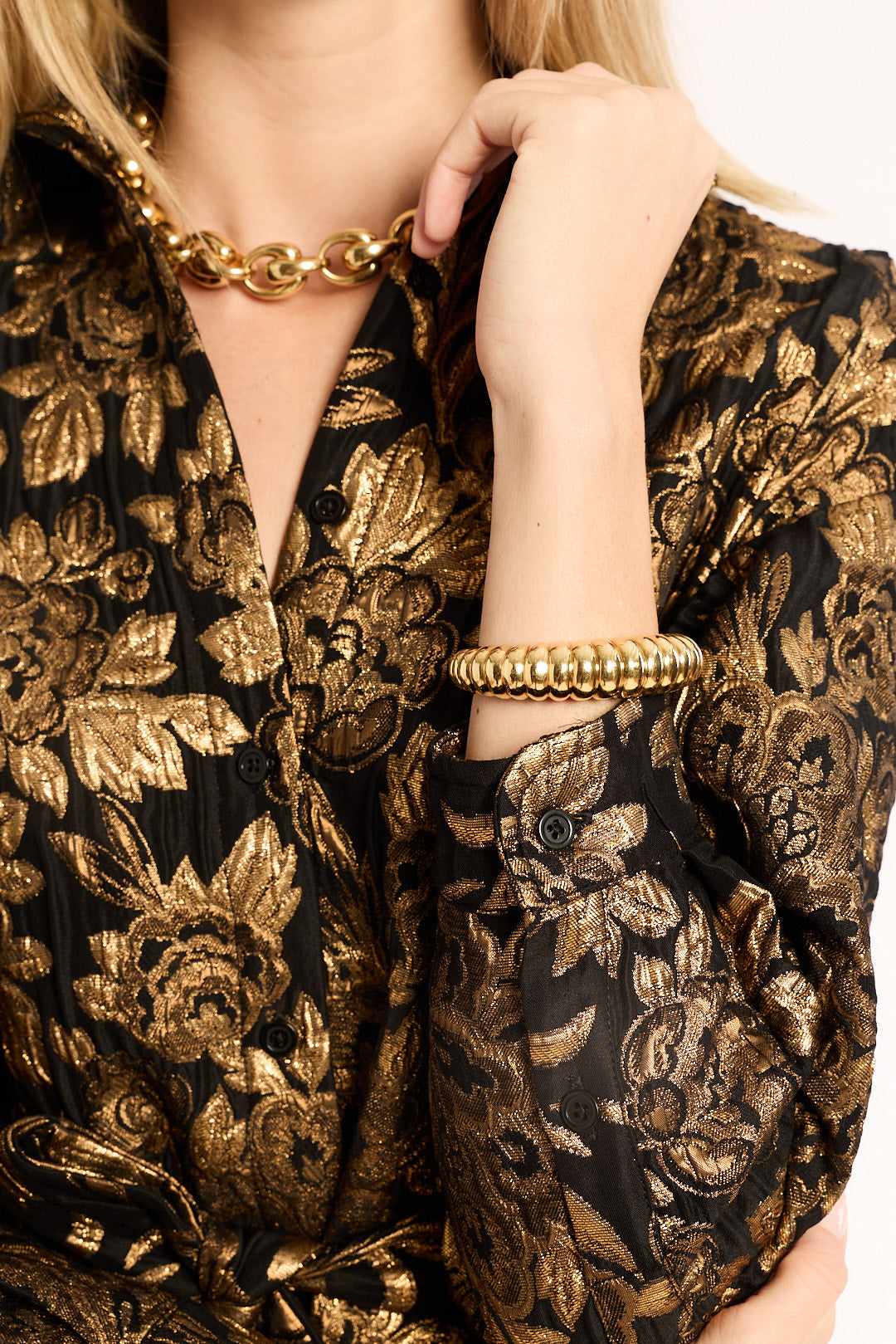 Person wearing a black and gold floral patterned outfit with jewelry.