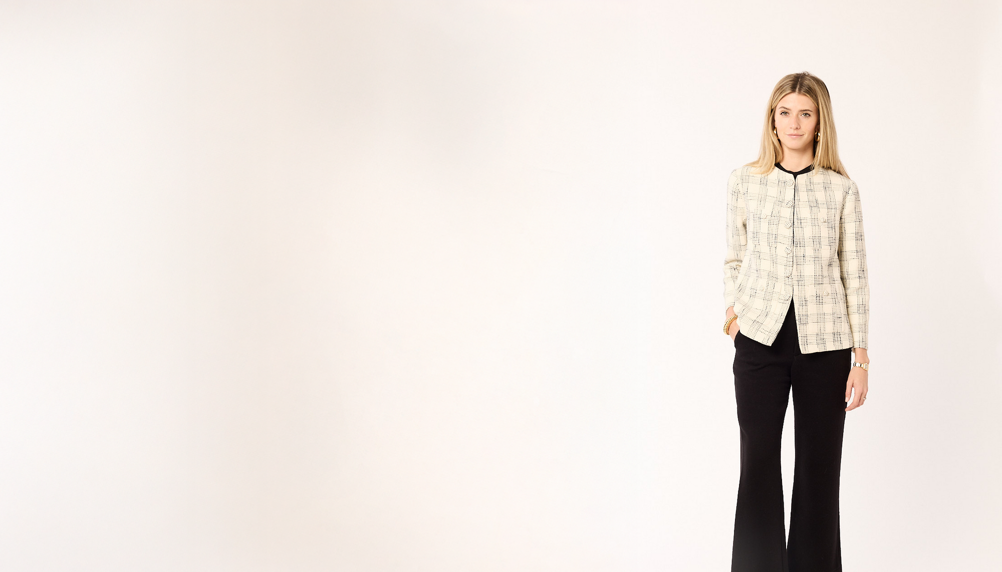 Woman in a cream and black blazer and black susie pants on a white background.