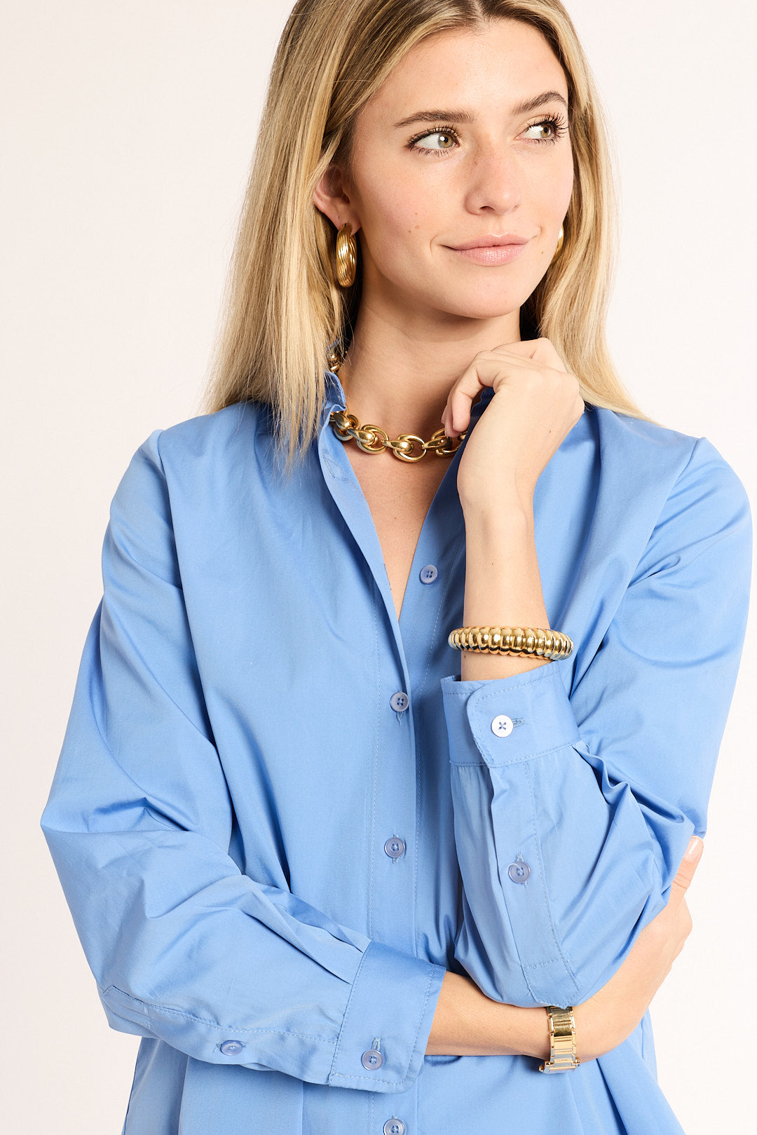 Woman wearing a blue shirt with gold jewelry on a beige background
