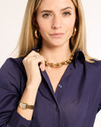 Woman wearing a gold chain necklace and watch, with a plain background