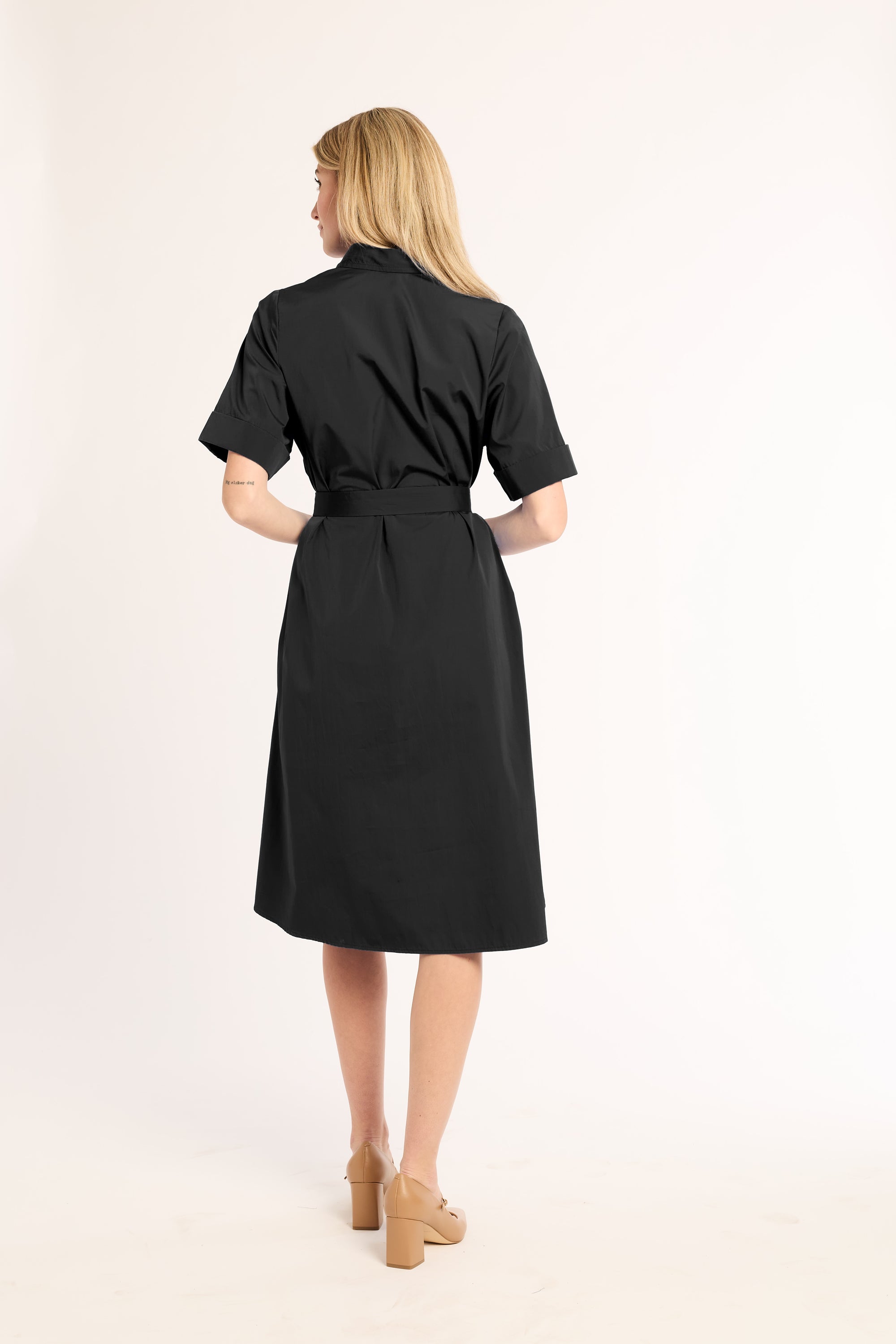 Woman wearing a black dress with a belt on a light pink background