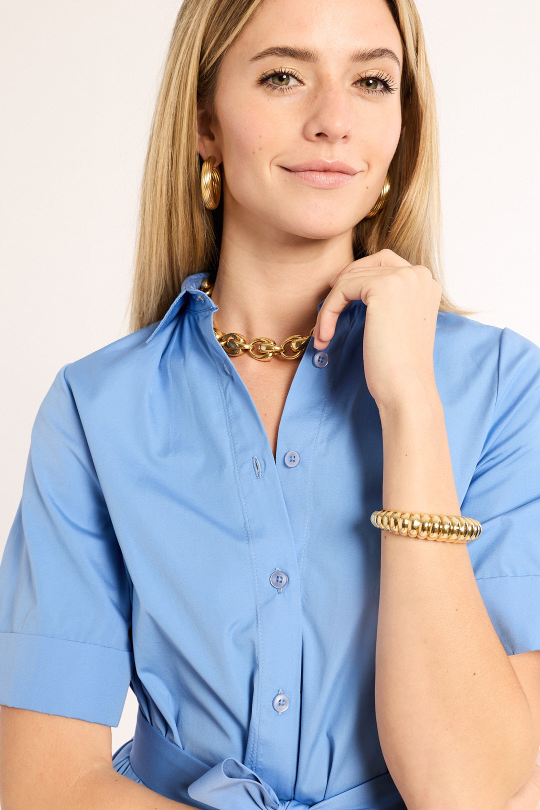 Woman wearing a blue shirt with gold jewelry on a beige background