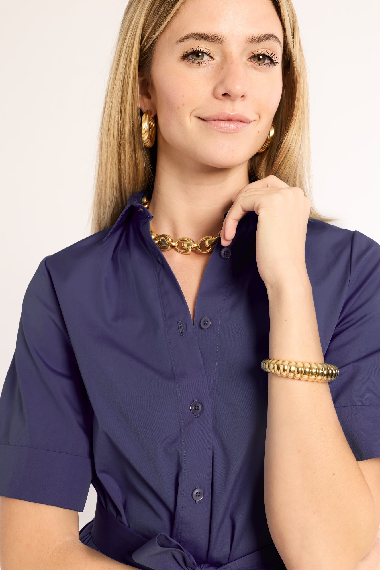 Woman wearing a navy dress with gold jewelry on a plain background