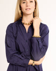Woman wearing a navy dress with gold jewelry on a plain background