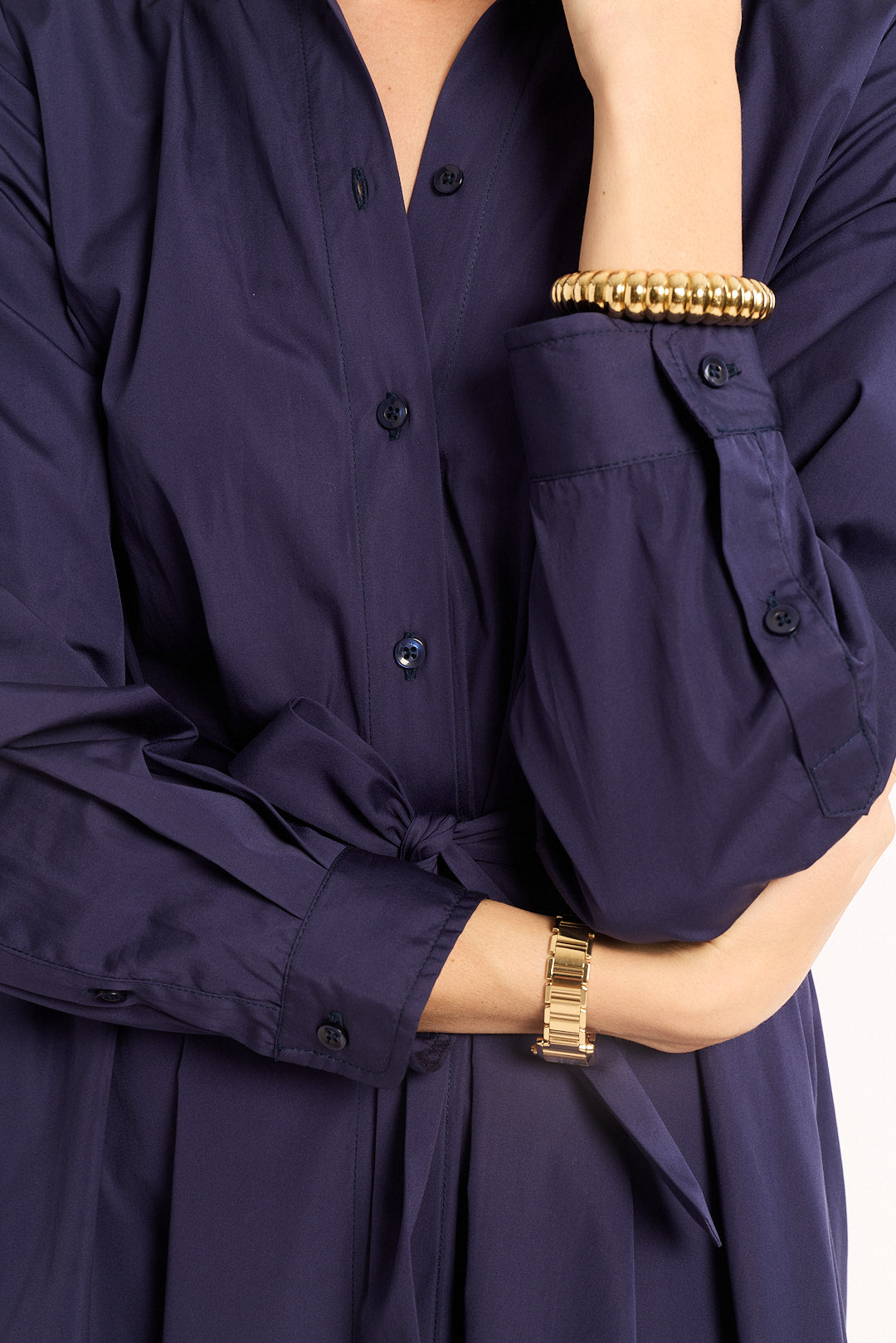 Navy blue shirt with a tie waist worn by a person, with gold bracelets on wrists.
