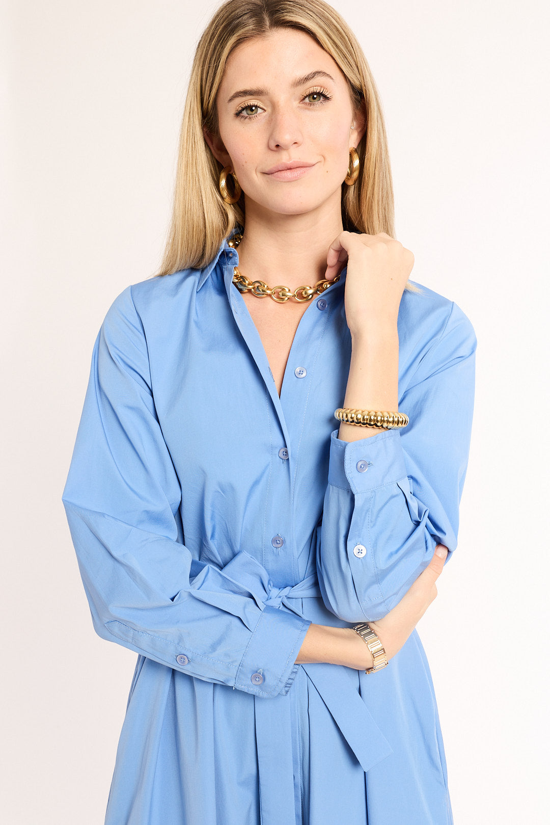 Woman wearing a light blue dress with gold jewelry on a plain background