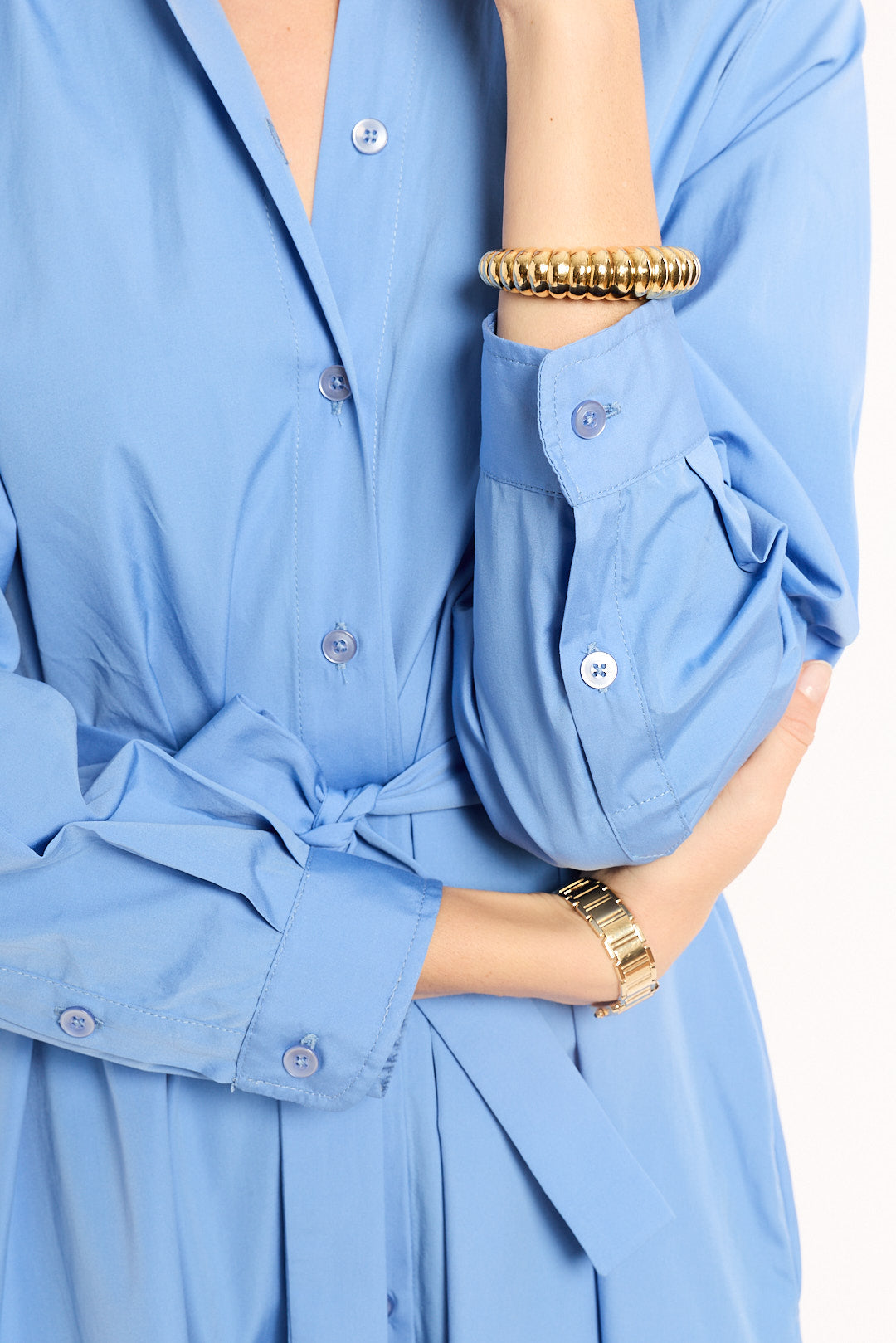 Close-up of a person wearing a light blue shirt with rolled-up sleeves and gold bracelets.
