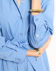Close-up of a person wearing a light blue shirt with rolled-up sleeves and gold bracelets.