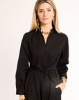 Woman wearing a black shirt with a tie waist on a plain background