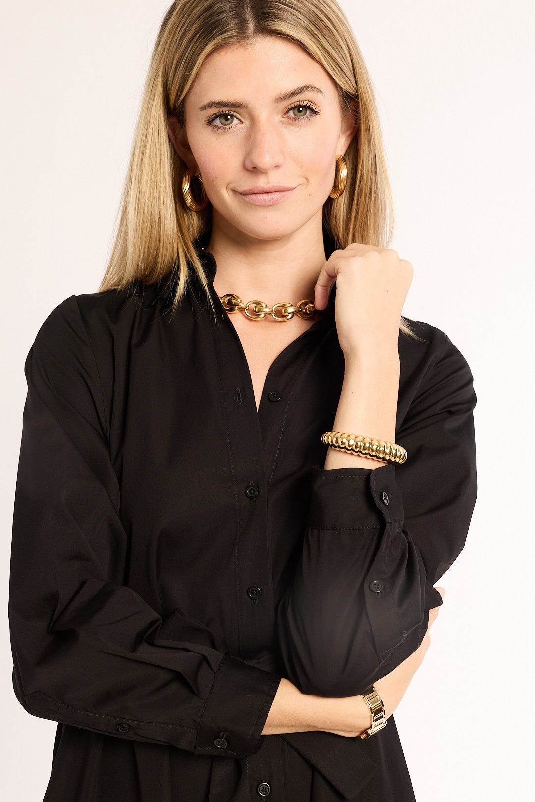Woman wearing a black shirt and gold jewelry on a plain background