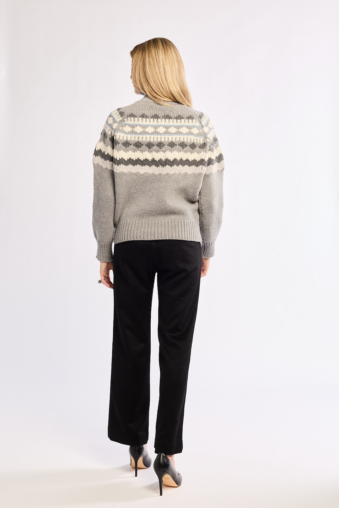 Person wearing a patterned sweater and black pants on a white background