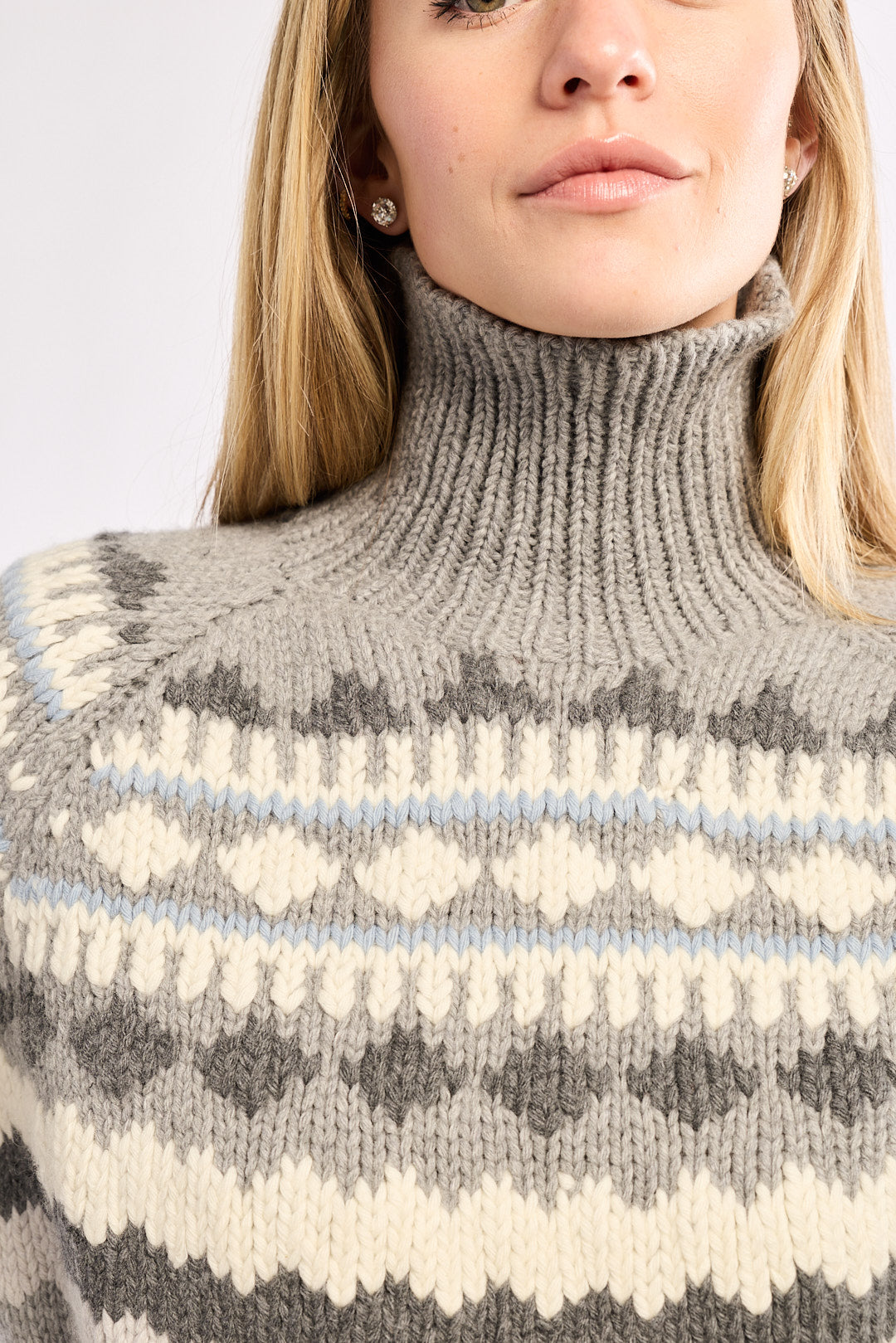 Person wearing a gray knit sweater with a patterned design on a plain background