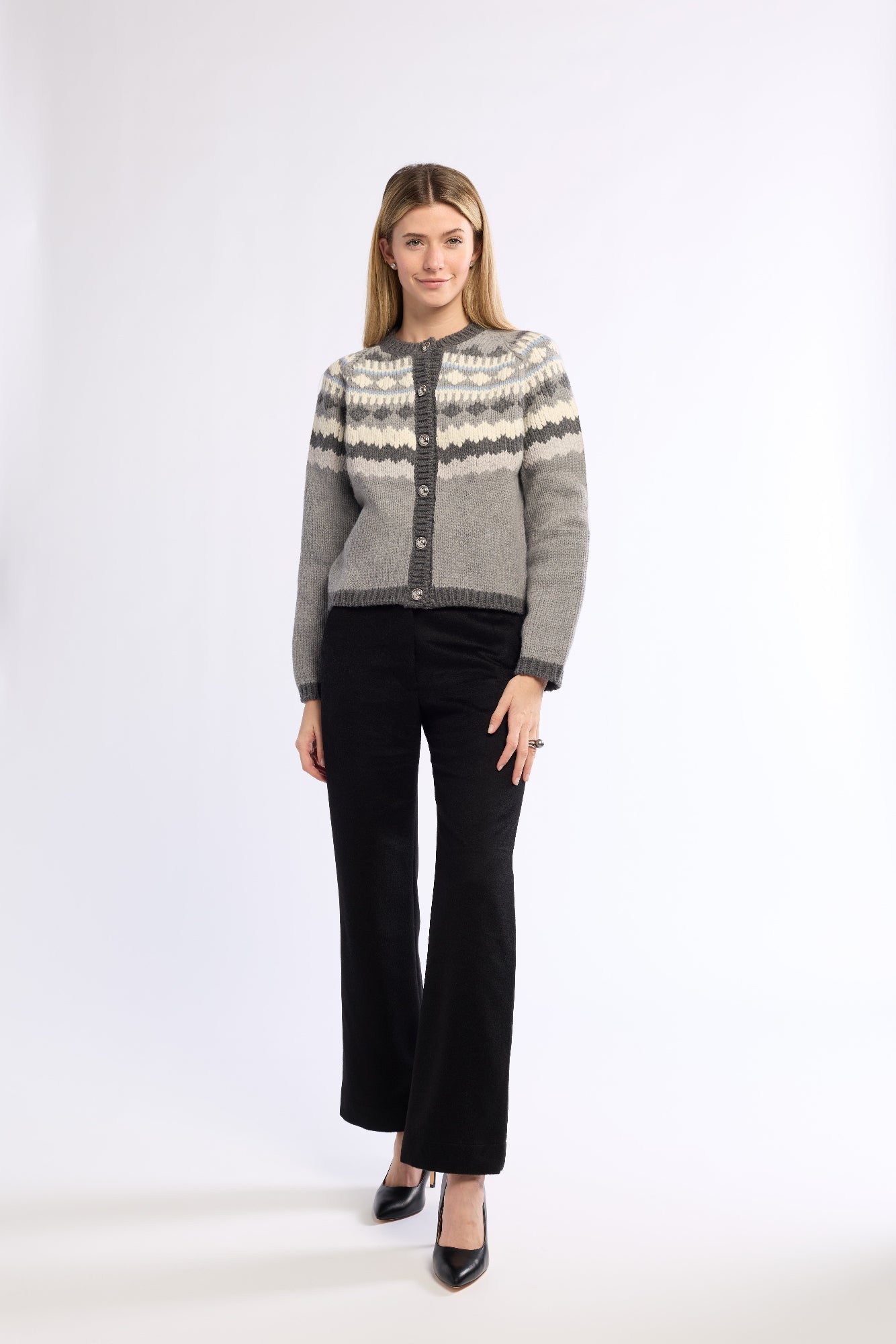 Woman wearing a gray patterned sweater and black pants and black shoes on a white background