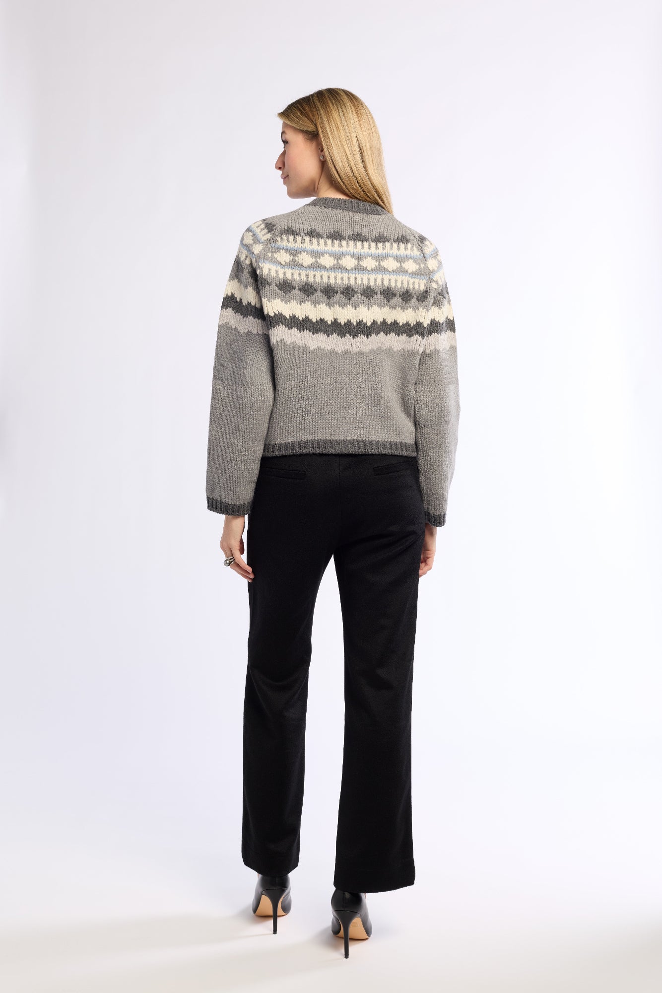 Woman wearing a grey patterned sweater and black pants on a white background